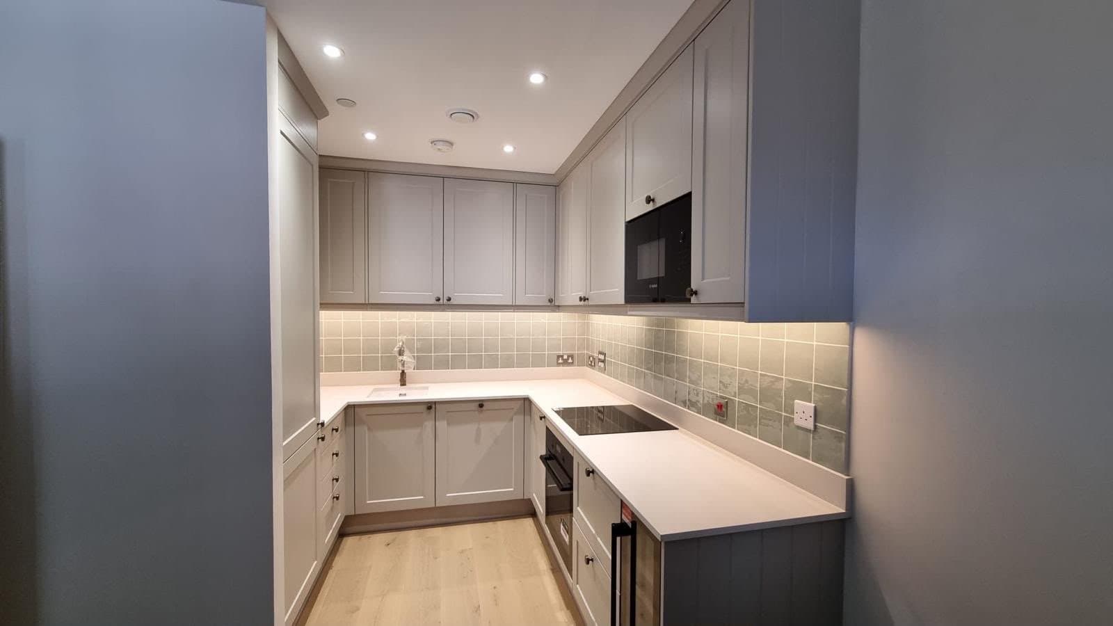 View into a finished SINA Kitchen Fitters kitchen: grey shaker units, built-in oven and microwave, white worktop and oak-effect floor
