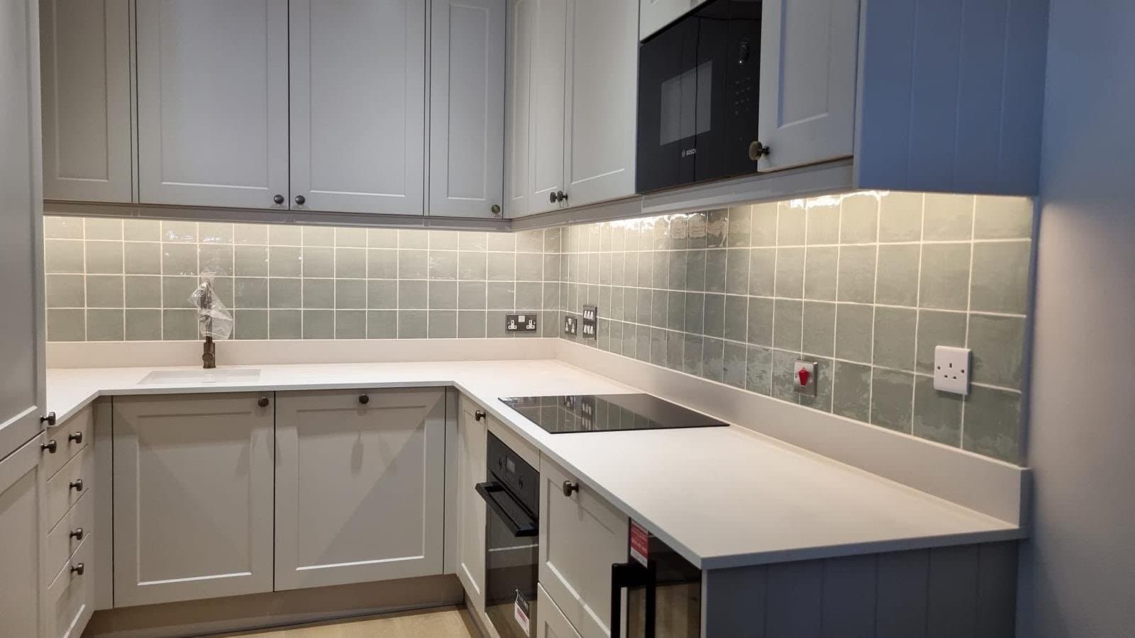 Finished kitchen fitted by SINA Kitchen Fitters: grey shaker units, white worktop, green tiled splashback and under-cabinet lighting