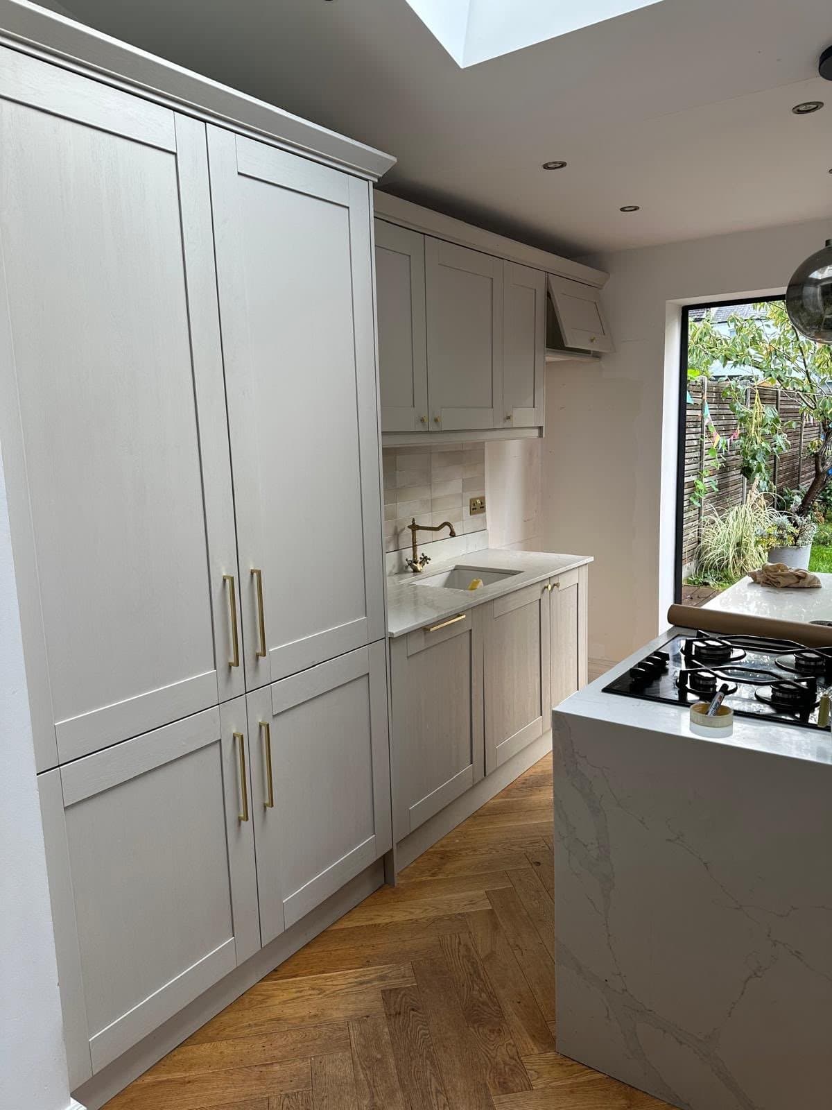 Finished kitchen fitted by SINA Kitchen Fitters: grey shaker units with brass-finish handles, a stone-effect peninsula with gas hob and a herringbone floor