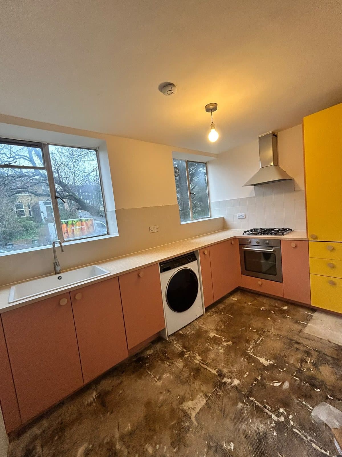 Finished kitchen fitted by SINA Kitchen Fitters: pink units, a yellow tall unit, gas hob and cooker hood
