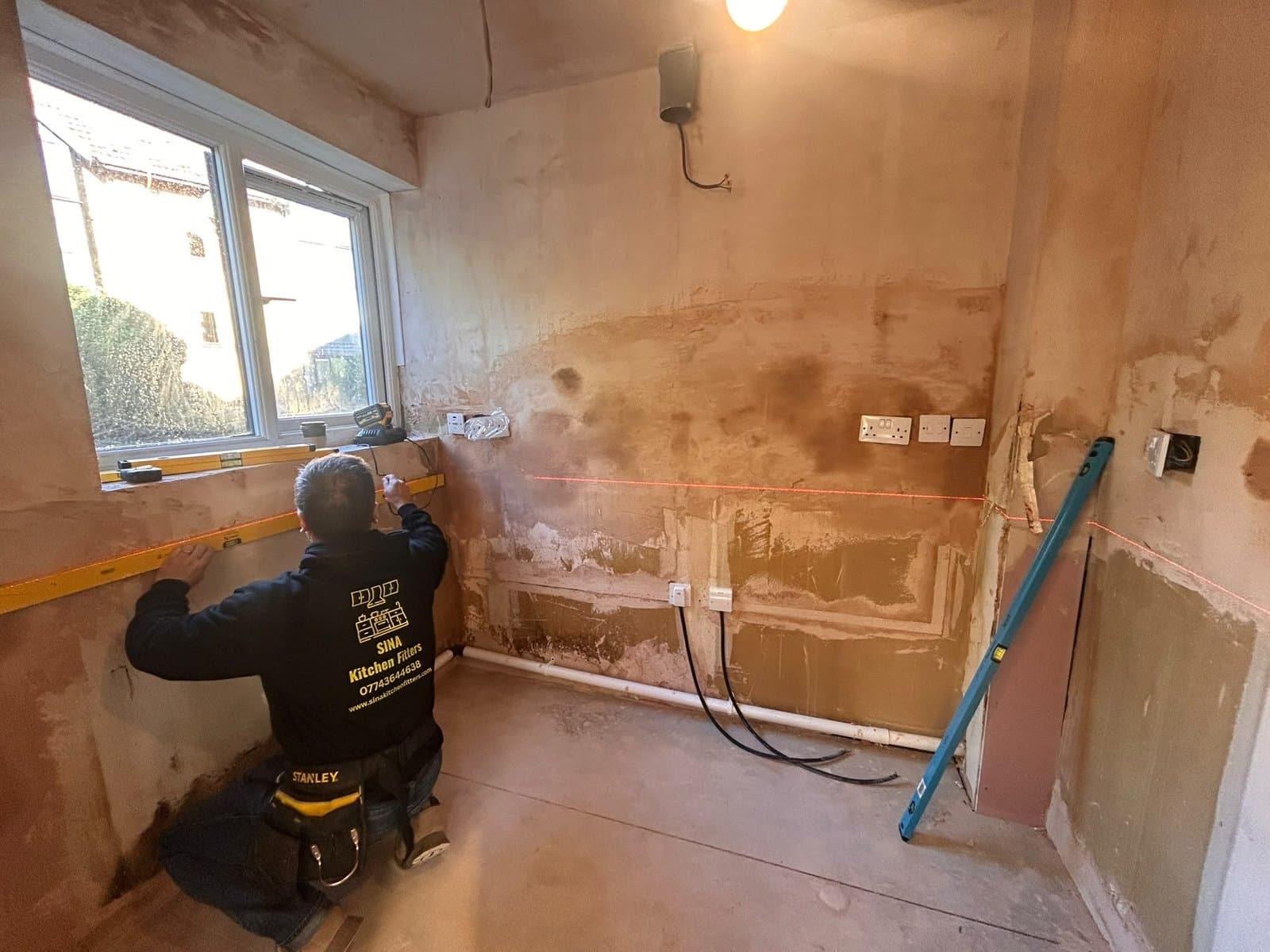 Kitchen fitter in a SINA Kitchen Fitters top marking level lines on a bare wall before installation