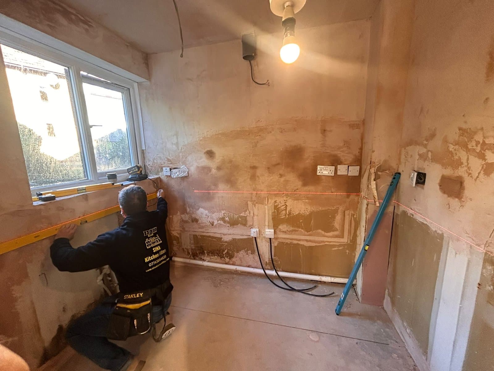 SINA Kitchen Fitters setting out a kitchen wall with a laser level before the units go in